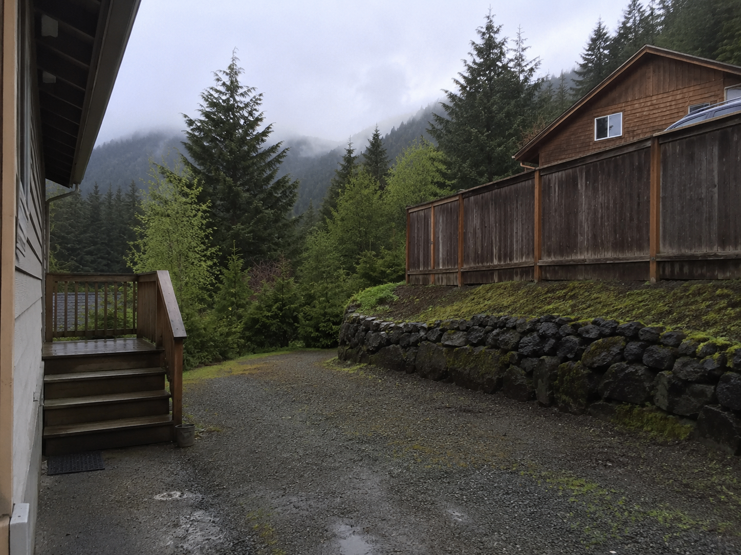 Juneau home exterior with gravel driveway and mountain forest backdrop